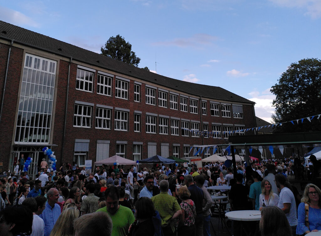 Schulgebäude des Stiftischen Gymnasiums Düren vom Schulhof aus mit vielen Menschen im Vordergrund.