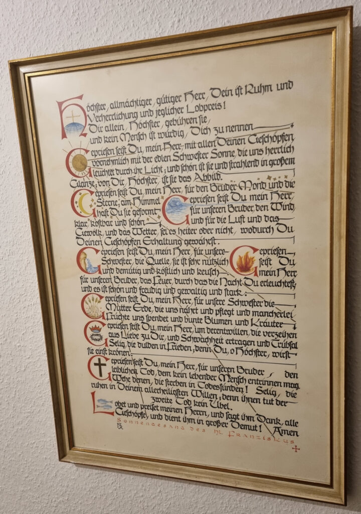 Bilderrahmen an der Wand enthält in Kalligraphie den Sonnengesang des Franz von Assisi